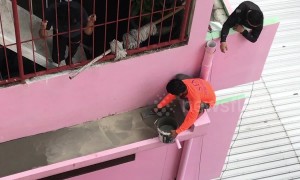 Thai man in flip-flops squats on 50ft high narrow ledge to do DIY home repairs