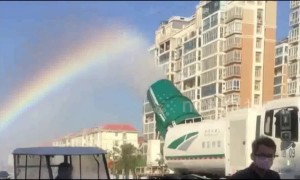 Lorry-mounted sprinkler leaves rainbow trail in the air behind it