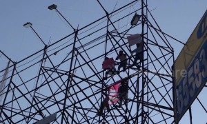Indian men scale a billboard scaffold in political protest