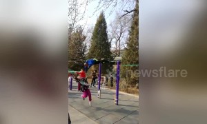 Old Chinese man swinging on horizontal bar knocks down girl walking by