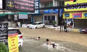 Boys go bodyboarding on flooded road in Thailand