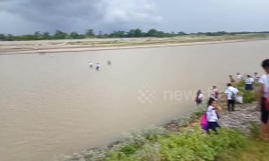 Children walk across a flooding river to attend school