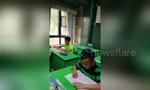 Chinese pupils balance plastic cups on heads while practising their handwriting