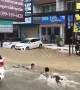 Boys go bodyboarding on flooded road in Thailand