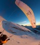 Paraglider Flies and Skis Over Golden Hour Mountains